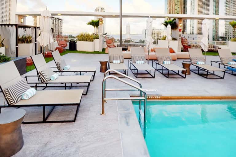 Rooftop pool deck with loungers, white umbrellas, and city skyline views at urban hotel