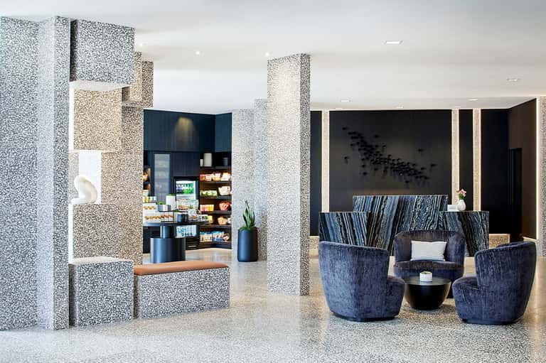 Contemporary hotel lobby with terrazzo columns, blue modern seating, and minimalist design aesthetic