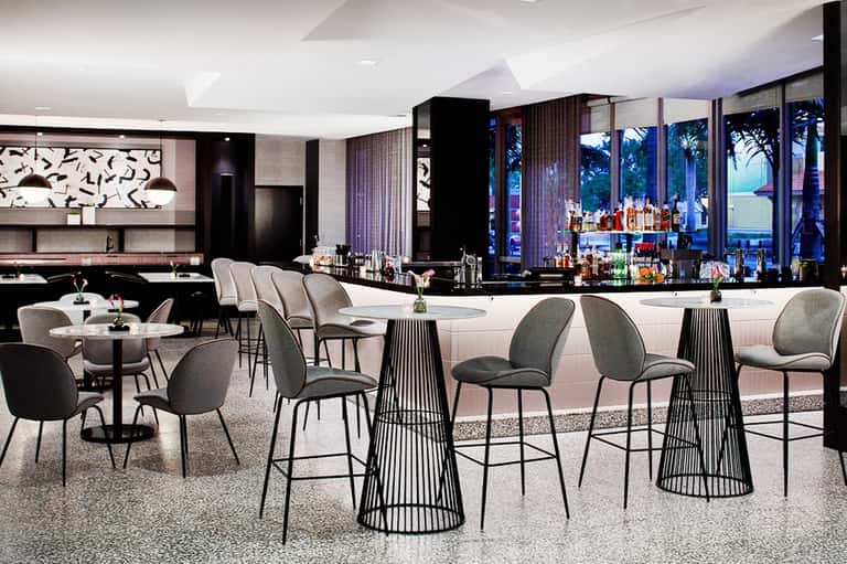Contemporary upscale bar lounge with modern seating, floor-to-ceiling windows overlooking beach and turquoise water