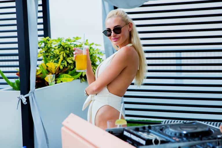 Woman in resort attire holding tropical drink by poolside cabana