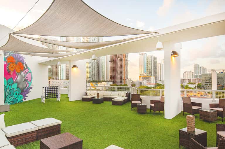 Rooftop lounge with shaded seating, artificial turf, contemporary furniture, and city skyline view