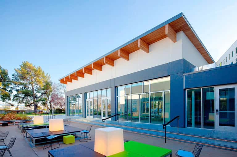 Modern resort building with blue exterior, wooden overhang, glass doors, and illuminated outdoor seating