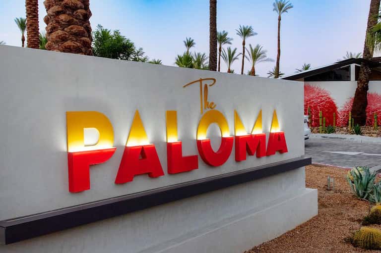 The Paloma resort entrance sign with illuminated yellow and red lettering and palm trees