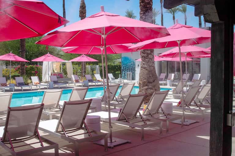 Resort pool area with bright pink umbrellas, beige lounge chairs, and palm trees