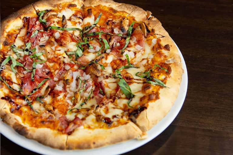 Wood-fired pizza with bacon, cheese, and fresh herbs on white plate