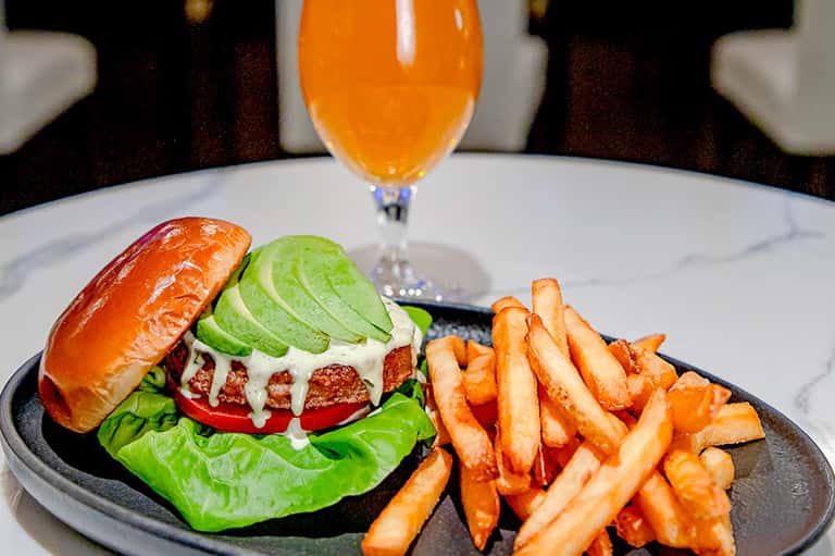 Gourmet burger with avocado slices, melted cheese, fresh greens, and fries served with orange juice