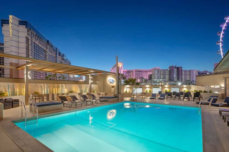 Illuminated rooftop pool at night with lounge chairs and downtown city skyline views