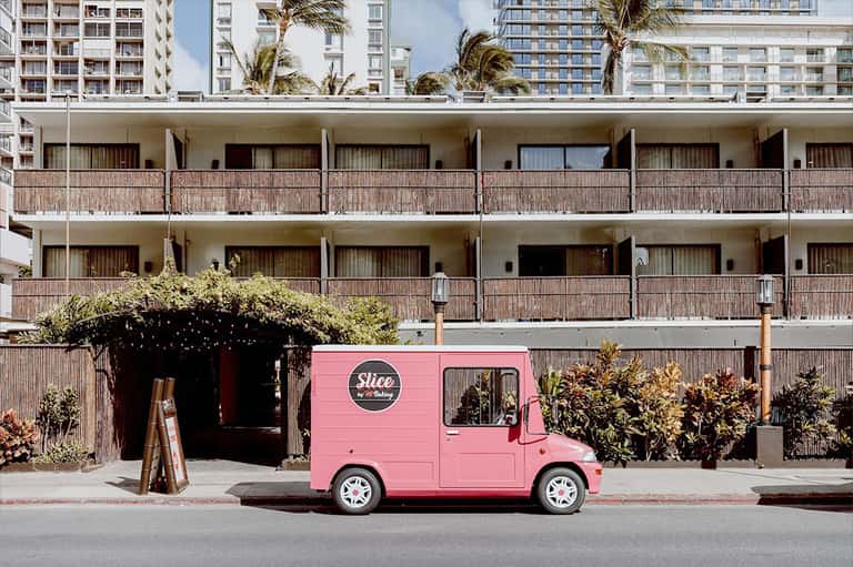 Pink food truck parked in front of modern hotel building with palm trees and residential towers
