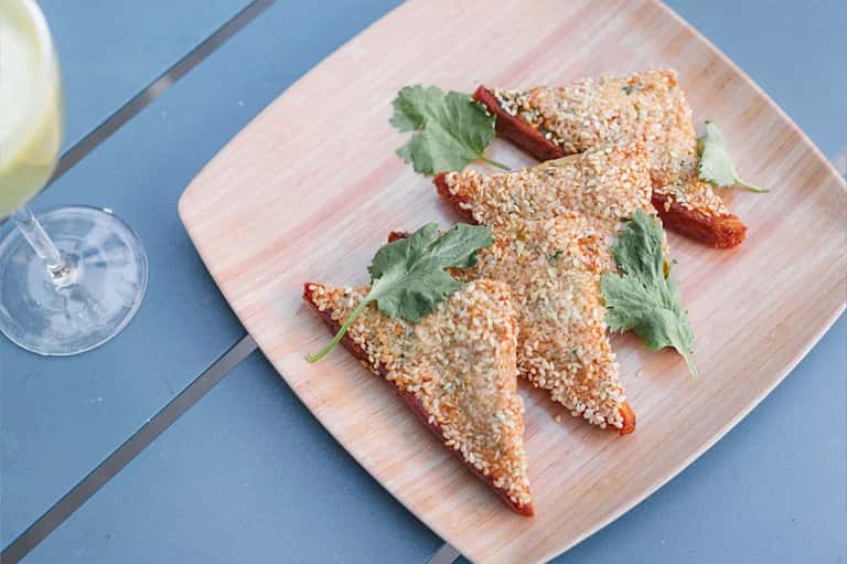 Gourmet appetizers with sesame coating and herbs on white wooden board next to cocktails