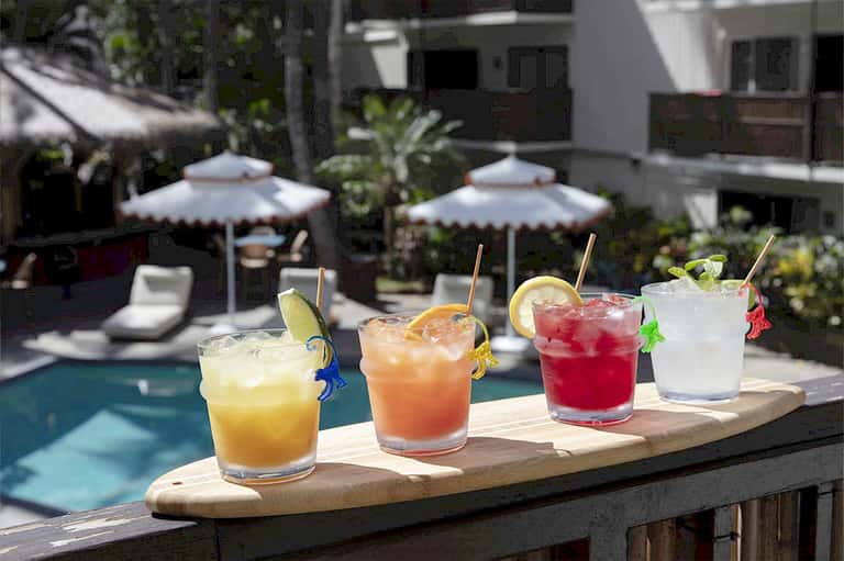 Four colorful tropical cocktails displayed poolside with umbrellas and garnishes