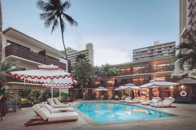Resort pool with red and white striped umbrellas, loungers, and palm trees