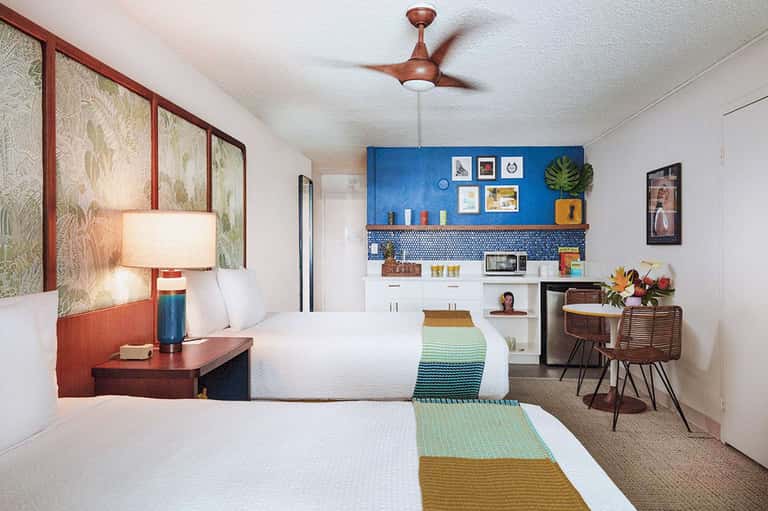 Colorful hotel guest room with two beds, kitchenette, blue accent wall, and modern furnishings