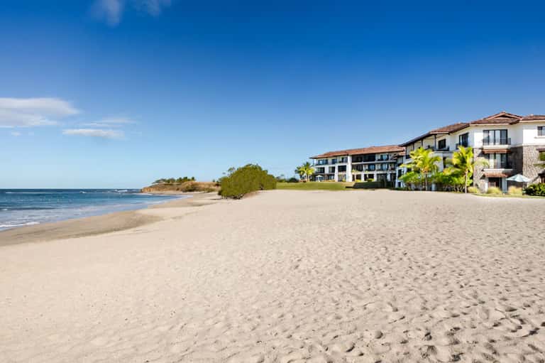 Beachfront property with sandy shore, residential buildings, and clear blue water