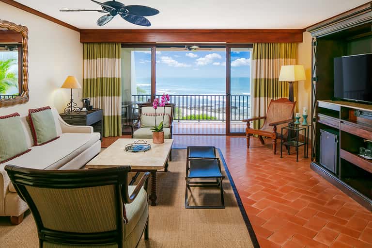 Beachfront resort suite with ocean view balcony, green curtains, and tropical setting