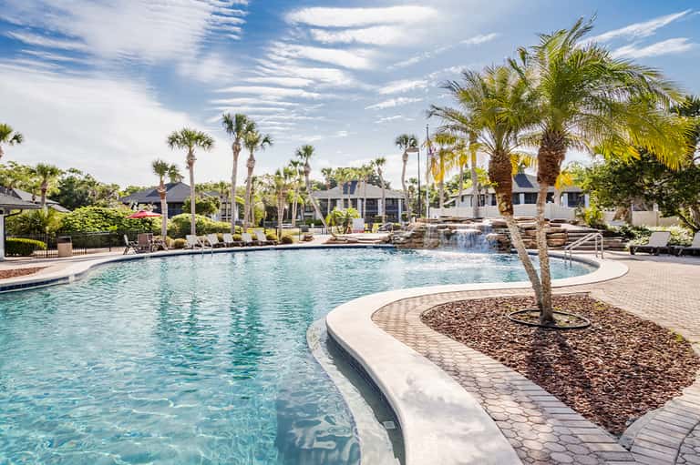 Luxurious resort pool with palm trees, lounge chairs, and elegant pool houses in background