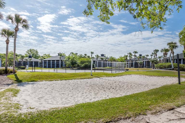 Sandy volleyball courts with nets surrounded by palm trees and green grass in resort community