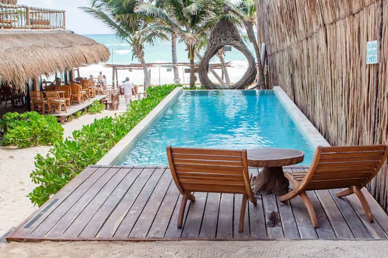 Beach-view infinity pool with wooden deck chairs, palm trees, and ocean horizon