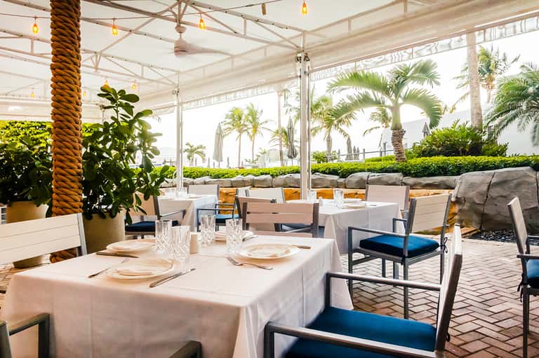 Elegant outdoor dining pavilion with white linens, palm trees, and ocean view in background