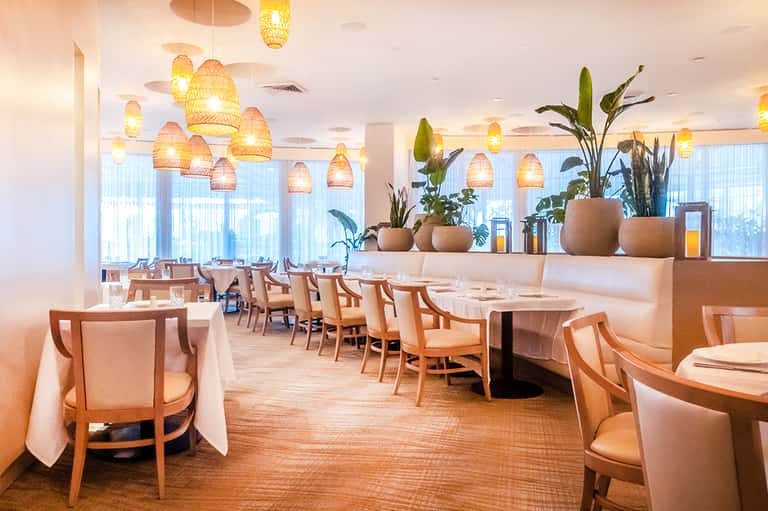 Elegant fine dining restaurant with woven pendant lights, potted plants, and white tablecloths
