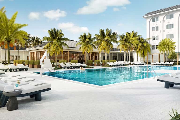 Tropical resort pool with palm trees, white lounge chairs, and modern architecture
