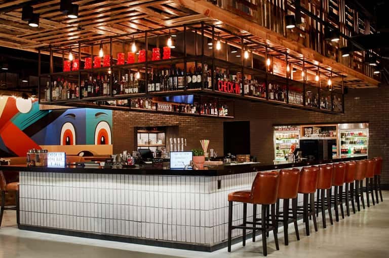 Contemporary restaurant bar with industrial design, red neon signage, wooden ceiling, and cognac leather stools
