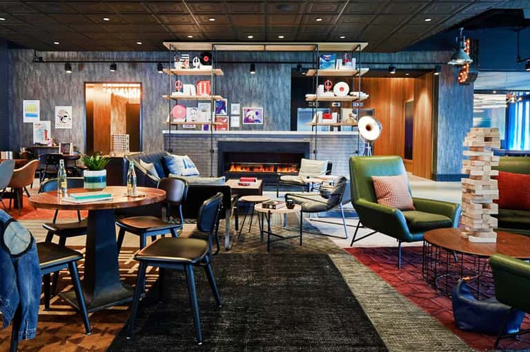 Contemporary hotel lobby with blue-gray walls, fireplace, colorful seating, round wooden table, and modern artwork on walls