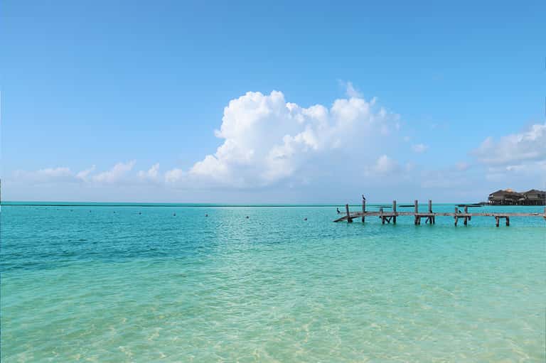 Turquoise tropical ocean with wooden pier and overwater bungalows under blue sky