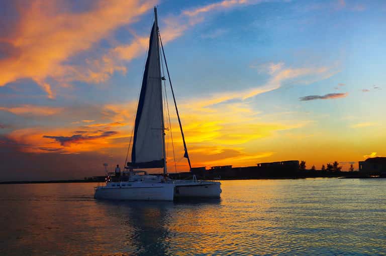 Sailboat anchored at sunset with golden sky reflecting on calm tropical water