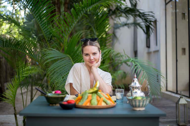 Woman dining al fresco surrounded by tropical palm plants and colorful fruit platters