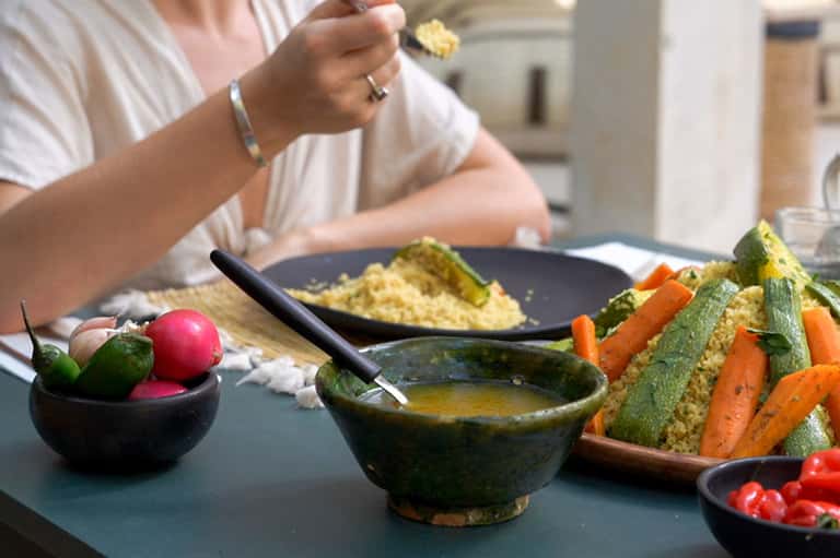 Person dining on healthy meal with couscous, vegetables, and sauce bowls