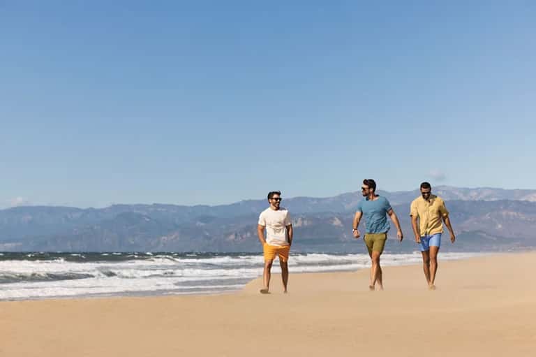 Three men jogging on beach with mountains in background and ocean waves