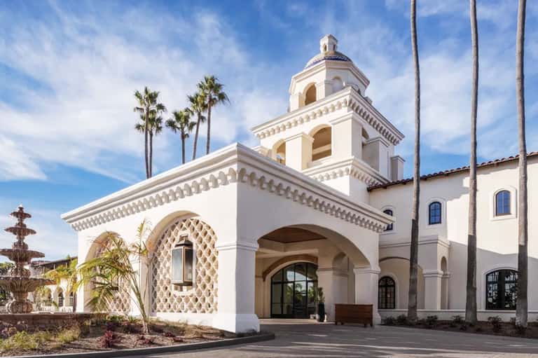 White Spanish colonial mission-style chapel with bell tower and tall palm trees