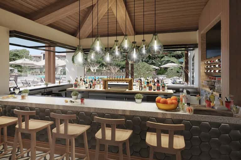 Upscale resort bar with pendant lights, wooden ceiling, bottles displayed, and outdoor seating visible
