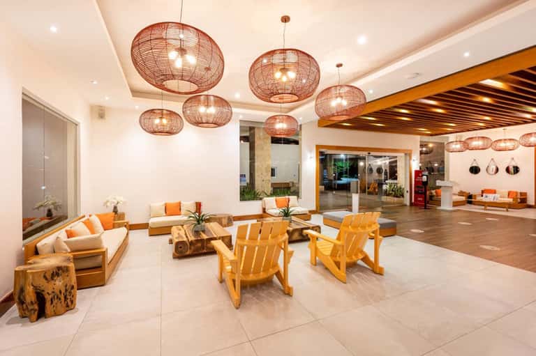Modern hotel lobby with orange accents, woven pendant lights, and wooden furniture