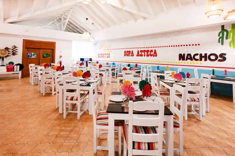 Casual dining room with colorful Mexican décor, white chairs, and ocean views