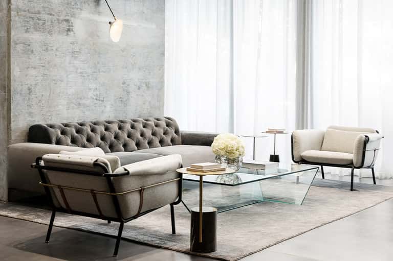 Contemporary living room with tufted sofa, modern chairs, glass coffee table, and concrete wall