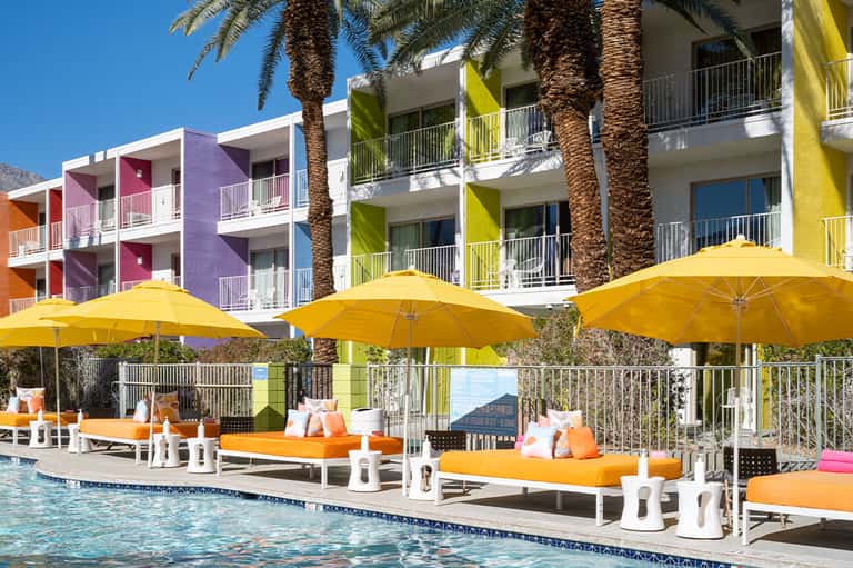 Colorful beachfront resort buildings with yellow umbrellas, orange loungers, and palm trees