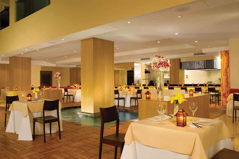 Elegant banquet hall with yellow walls, wood pillars, round tables with white linens, and centerpiece flowers