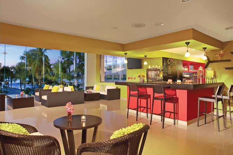 Vibrant hotel lobby with lime green ceiling, red bar, and ocean views through windows