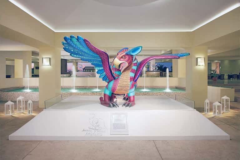 Exhibition space with colorful sculptural bird installation and white platform in bright minimalist interior