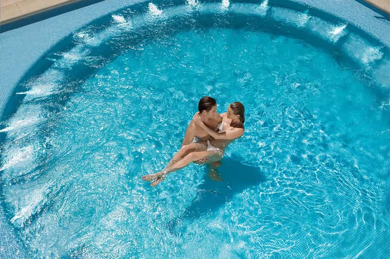 Adult and child swimming together in bright turquoise resort pool on sunny day