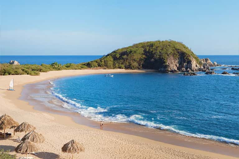 Scenic tropical beach cove with golden sand, turquoise water, lush green hilltop, and gentle waves