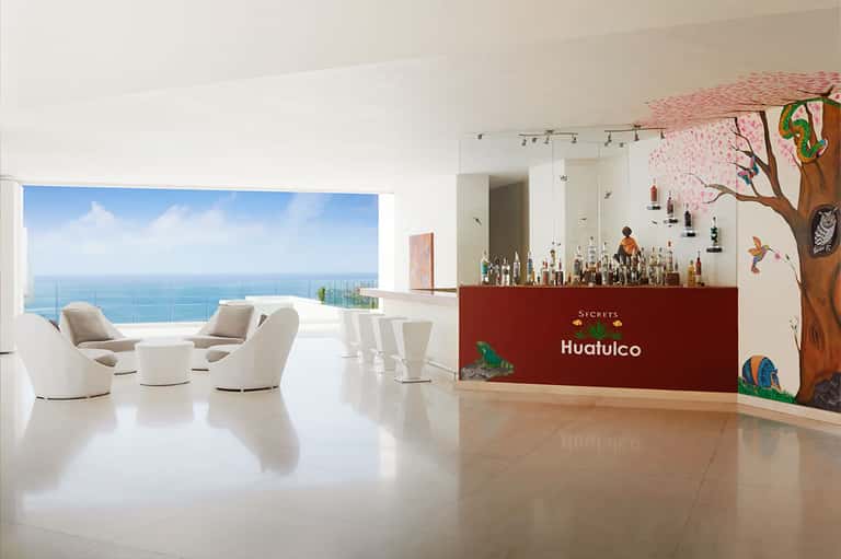 Secrets Huatulco resort lobby with ocean views, white furniture, and tropical-themed bar area