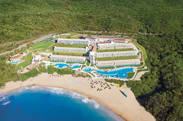 Aerial view of large beachfront resort with multiple pools and buildings nestled in forest