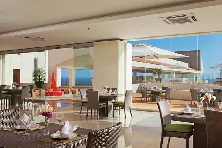 Upscale restaurant dining room with ocean views, modern brown wicker chairs, and outdoor terrace
