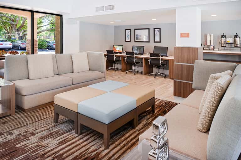 Modern lobby lounge with beige sectional seating, work station, contemporary artwork, and bright natural lighting