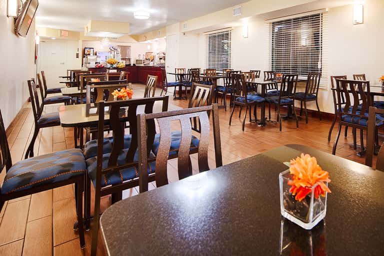 Hotel dining area with wooden tables, chairs, and open kitchen concept