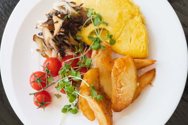 Plated omelet with mushrooms, potatoes, fresh tomatoes, and microgreens on white dish