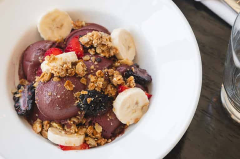 Gourmet chocolate ice cream dessert topped with granola, banana slices, and berries on white plate