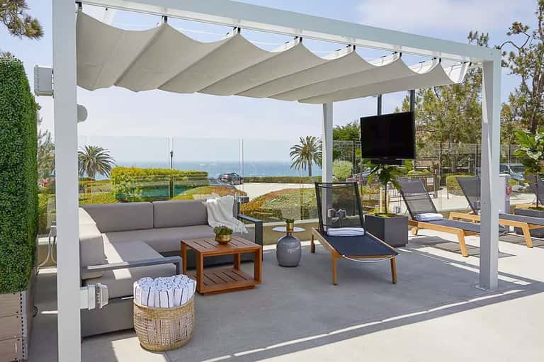Luxury poolside lounge with white pergola, gray seating, ocean views, and modern landscaping
